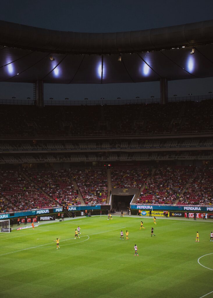 An exciting night football game under bright stadium lights with a large cheering audience.